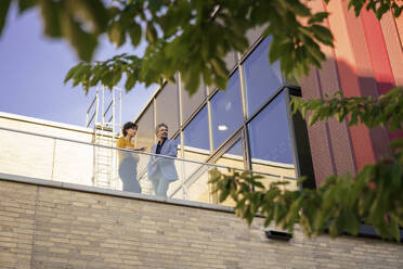 Senior businessman discussing with colleague on balcony at sunny day - JOSEF21825