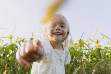 Happy girl holding crop in front of plants - NDEF01229