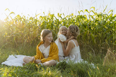 Girl with mother embracing and kissing daughter in field - NDEF01233