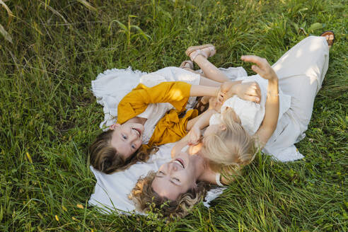 Cheerful mother having fun with daughters lying on grass - NDEF01235