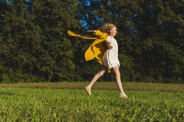 Cheerful girl jumping on grass in front of trees - NDEF01244