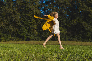Fröhliches Mädchen springt auf Gras vor Bäumen - NDEF01244