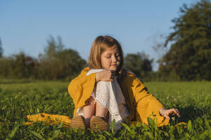 Lächelndes Mädchen, das an einer Blume riecht und im Gras sitzt - NDEF01256