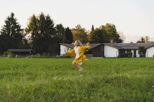 Cheerful girl running on grass in front of houses - NDEF01263