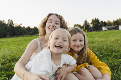 Happy mother and daughters enjoying together on grass - NDEF01268