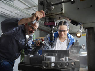 Apprentice spraying lubricant on drill bit by instructor in workshop - CVF02588