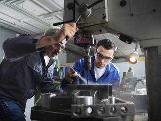 Instructor assisting trainee spraying lubricant on machine in workshop - CVF02589