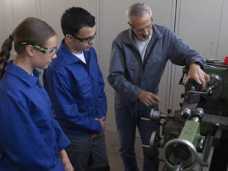 Trainees with instructor explaining lathe machine at workshop - CVF02590