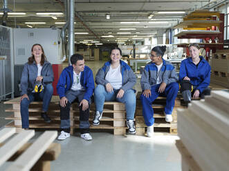Glückliche Auszubildende sitzen in der Werkstatt auf Paletten zusammen - CVF02591