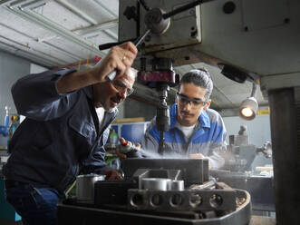 Instructor with trainee spraying lubricant on drill bit at workshop - CVF02593