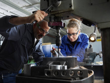 Focused trainee working with instructor near machine at workshop - CVF02597