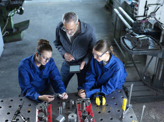 Instructor holding tablet PC teaching trainees using CNC tools at workshop - CVF02603