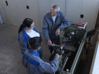 Instructor discussing with apprentices standing near lathe machine at workshop - CVF02608