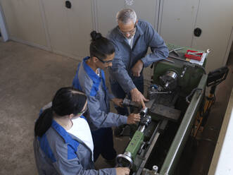 Instructor giving training to apprentices over lathe machine at workshop - CVF02611