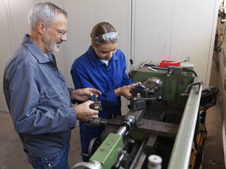 Trainee working with instructor standing near lathe machine at workshop - CVF02621