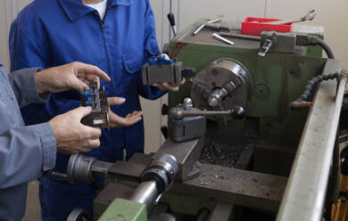 Trainee and instructor holding machine parts near lathe at workshop - CVF02623