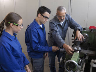 Instructor guiding apprentices using lathe at workshop - CVF02644