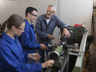 Instructor discussing with trainees over lathe at workshop - CVF02645