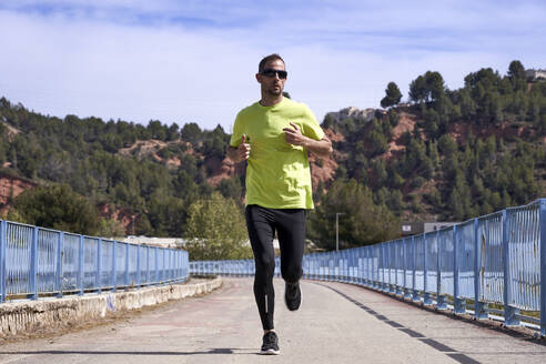 Aktiver Mann mit Sonnenbrille beim Joggen auf der Brücke - VEGF06209