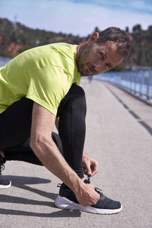 Man crouching and tying shoelace on sunny day - VEGF06210