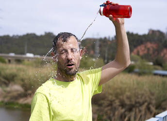 Mann mit geschlossenen Augen spritzt sich Wasser aus einer Flasche ins Gesicht - VEGF06220