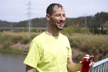 Lächelnder Mann steht mit geschlossenen Augen und hält eine Wasserflasche - VEGF06221