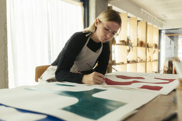 Blonder Künstler malt mit Pinsel am Schreibtisch im Atelier - EBSF03955