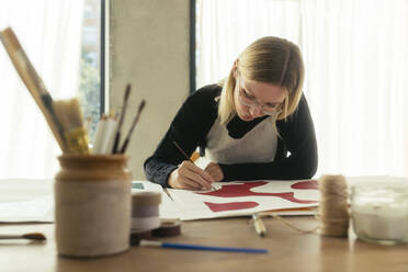 Blond artist painting on canvas at desk in studio - EBSF03956