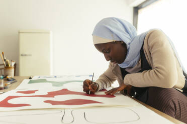 Artist wearing headscarf painting with brush in studio - EBSF03958