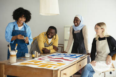 Lachende Künstler mit Bildern auf dem Schreibtisch im Atelier - EBSF03959