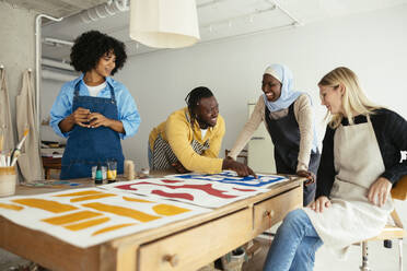 Lächelnde Künstler, die über Gemälde auf dem Schreibtisch im Atelier diskutieren - EBSF03960