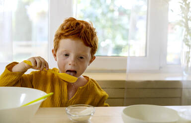 Boy eating sugar from spatula in kitchen at home - MBLF00036