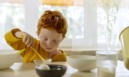 Junge mischt Zucker in einer Schüssel auf dem Esstisch zu Hause - MBLF00037