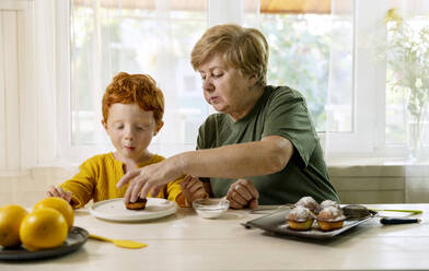 Großmutter serviert ihrem Enkel am Esstisch in der Küche ein Törtchen - MBLF00044