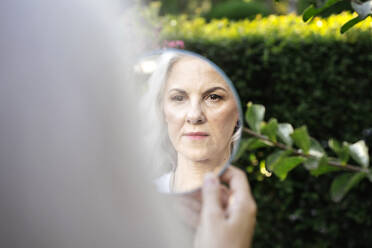 Mature woman with gray hair looking at reflection in mirror - YBF00275