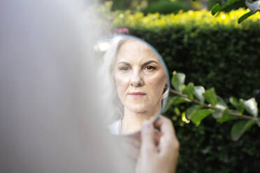 Reife Frau mit grauem Haar betrachtet ihr Spiegelbild im Spiegel - YBF00275