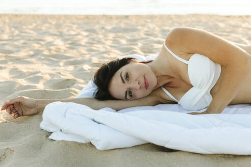 Smiling woman lying on blanket at beach - SIF01036