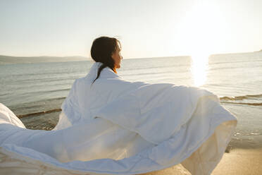 Unbekümmerte Frau mit Decke am Strand an einem sonnigen Tag - SIF01056