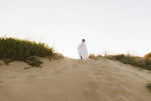 In eine Decke eingewickelte Frau steht am Strand unter dem Himmel - SIF01059