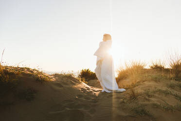 Frau in Decke eingewickelt am Strand stehend an einem sonnigen Tag - SIF01060