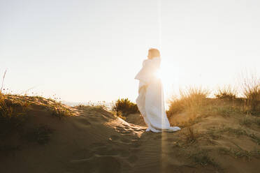 Woman wrapped in blanket standing at beach on sunny day - SIF01060