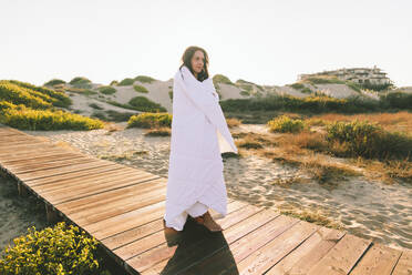 In eine Decke eingewickelte Frau auf der Promenade am Strand stehend - SIF01061