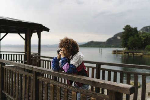 Frau beim Fotografieren mit Kamera vor einem See - BOYF02018
