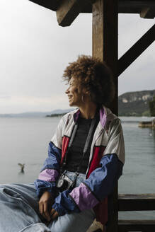Happy woman sitting on railing in front of lake - BOYF02035