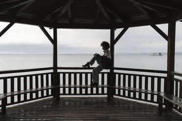 Junge Frau mit Buch auf Geländer unter Pavillon sitzend - BOYF02038