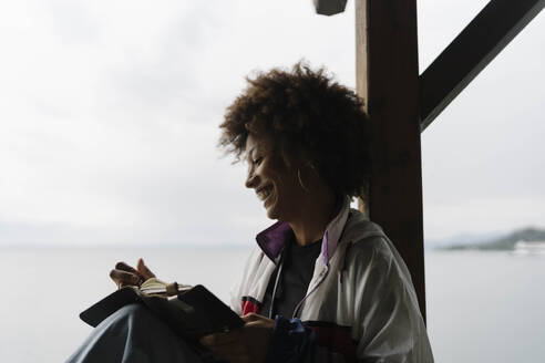 Happy young woman writing in book near lake - BOYF02041