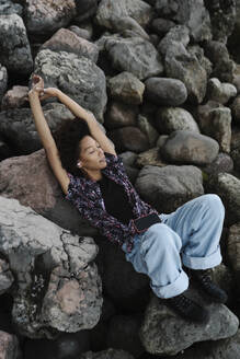 Young woman with arms raised relaxing on rocks - BOYF02058