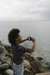 Junge Frau fotografiert mit Smartphone vor einem See - BOYF02061