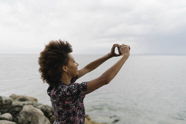 Glückliche junge Frau beim Fotografieren mit Smartphone vor einem See - BOYF02062