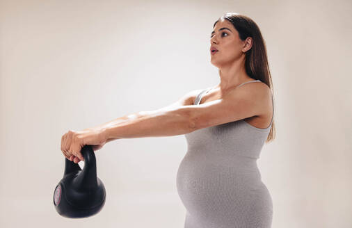 Eine Schwangere im dritten Trimester konzentriert sich auf Fitness und Wohlbefinden. Sie hebt Gewichte, dehnt sich und macht Übungen für einen gesunden Körper während der Schwangerschaft. Selbstfürsorge und pränatale Pflege sind für die werdende Mutter von größter Bedeutung. - JLPSF30875